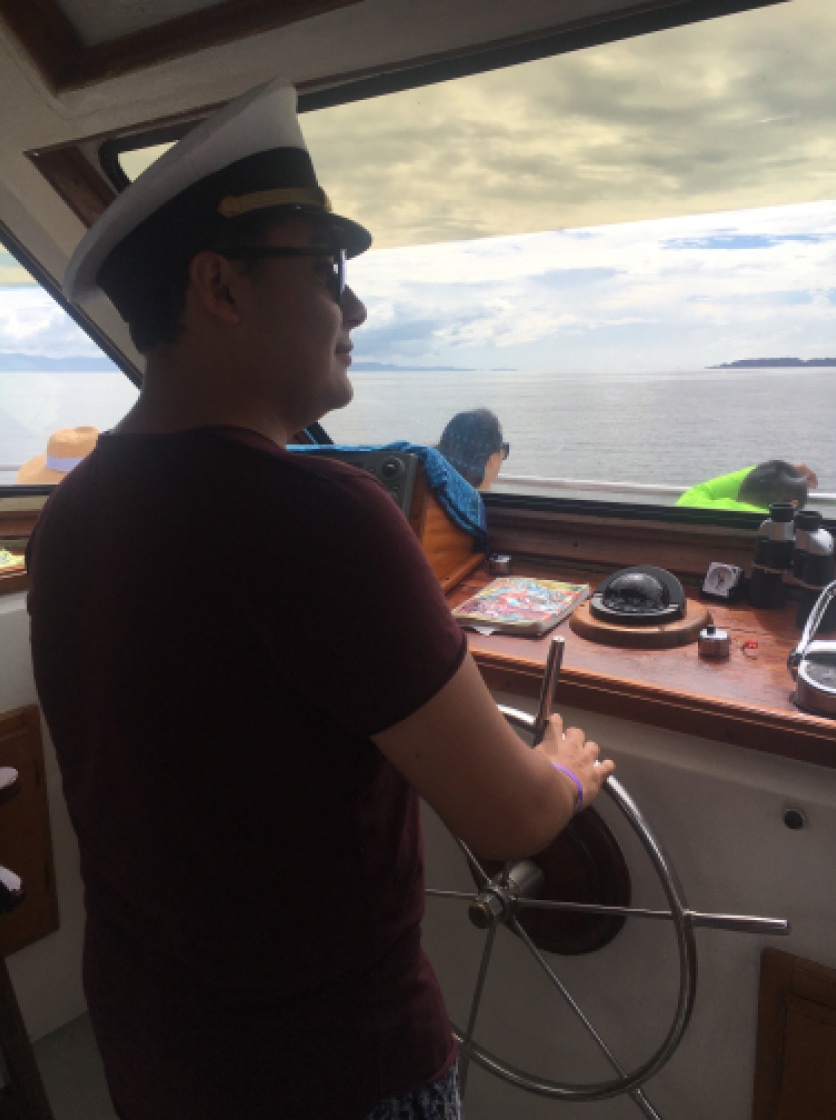 Yamil wearing a captain's cap at the helm of a boat, looking out over the sea.